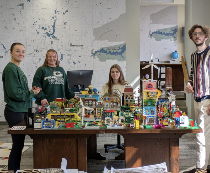 Students cluster around a colorful city built with LEGO bricks.