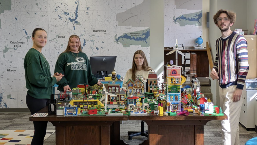 Students cluster around a colorful city built with LEGO bricks.