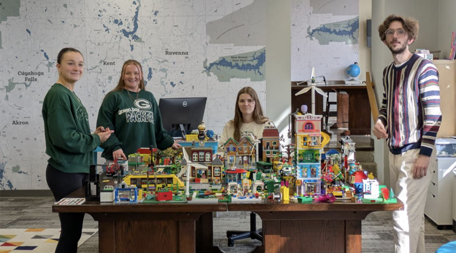Students cluster around a colorful city built with LEGO bricks.
